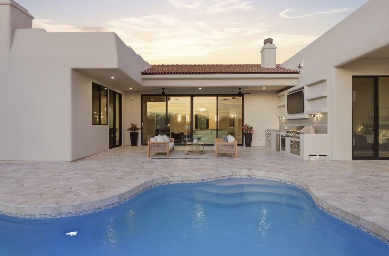 Covered patio with lounge seating and a built-in outdoor kitchen opening onto the pool at sunset