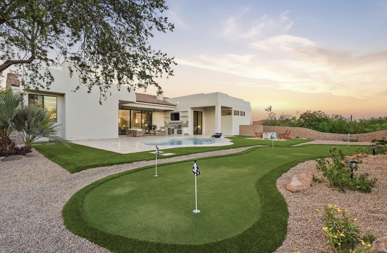 Wide view of a finished backyard with a pool, putting green, and desert landscaping