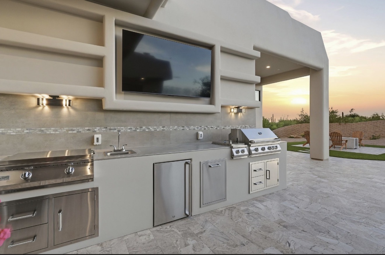 Built-in outdoor kitchen with a grill and travertine patio beside the pool